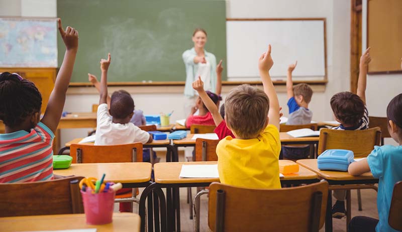 Photo of students in a classroom raising hands